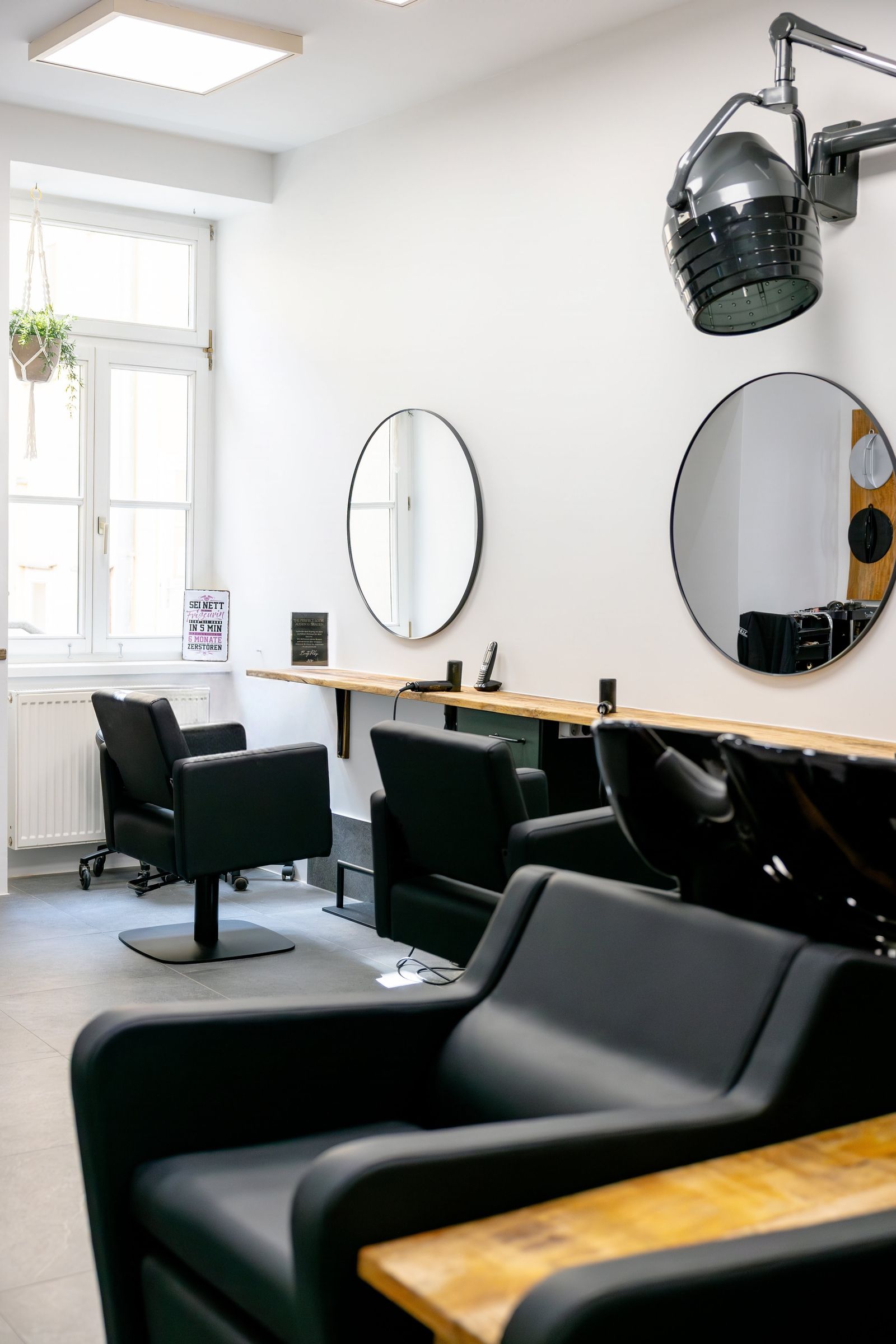 Heller HAARKUNSTWERK Salon mit schwarzen Sesseln und runden Spiegeln